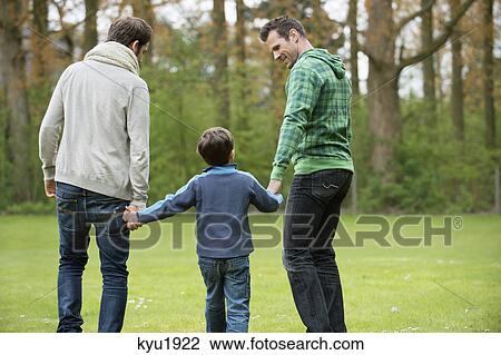 Stock Image - Rear view of a boy walking with two men in a park. Fotosearch