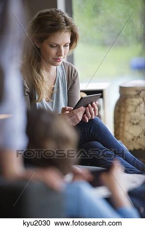Stock Image - Woman reading electronic book with her children at home. Fotosearch