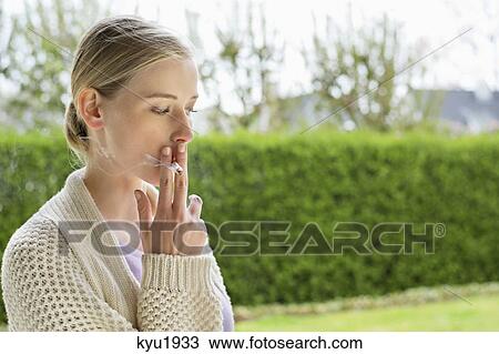 Stock Image - Woman smoking cigarette in park. Fotosearch