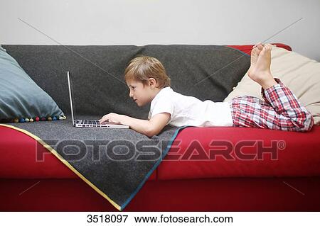 5 years old boy looking at a computer, lying on a sofa View Large Photo Image Stock Photo - 5 years old boy looking at a computer, lying on a sofa. Fotosearch