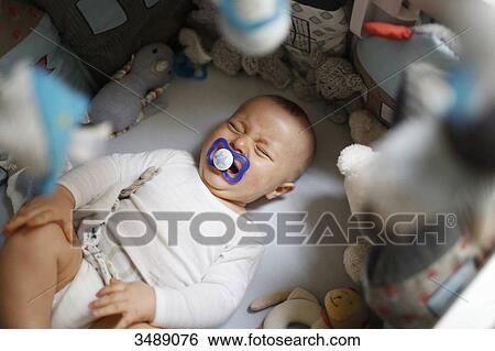 Stock Photograph - 8 months baby boy crying in his bed. Fotosearch