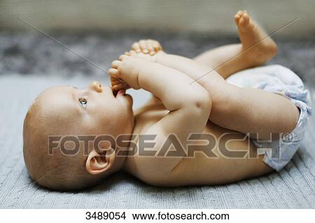 Picture - 8 months baby boy lying down and playing with his feet. Fotosearch