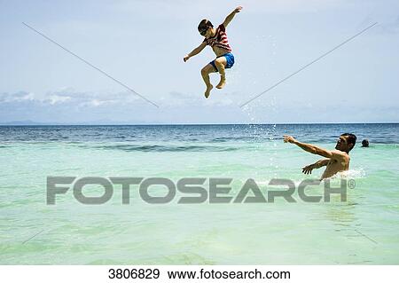 Stock Photo - A kid jumping in the sea with his father, Anse Figuier, Martinique, France. Fotosearch