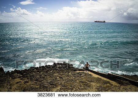 Stock Image - A man looking at a cargo, Gosier island, Guadeloupe, France. Fotosearch