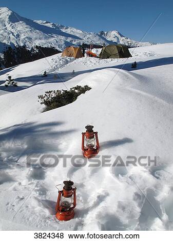 Austria, North tirol, Stubai alps, Fotsch valley, 2 oil lamps are placed in the fresh snow while in the background one sees 2 large camping tents in the snow in the middle of the mountains View Large Photo Image Stock Photo - Austria, North tirol, Stubai alps, Fotsch valley, 2 oil lamps are placed in the fresh snow while in the background one sees 2 large camping tents in the snow in the middle of the mountains. Fotosearch
