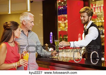 Stock Photo - Bartender serving drink to a couple at bar counter. Fotosearch