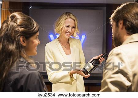 Picture - Bartender showing a wine bottle to customers. Fotosearch