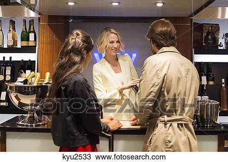 Stock Image - Bartender showing a wine bottle to customers. Fotosearch