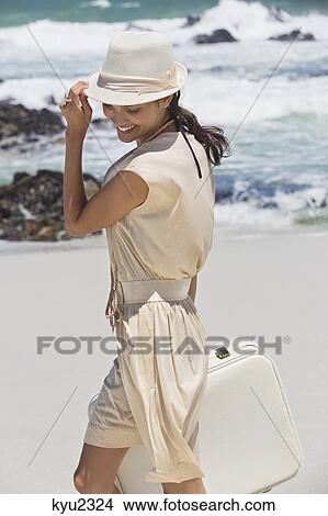 Picture - Beautiful woman carrying a suitcase on the beach. Fotosearch