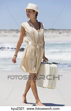 Stock Image - Beautiful woman carrying a suitcase on the beach. Fotosearch