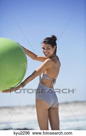 Stock Photograph - Beautiful woman holding a fitness ball on the beach. Fotosearch