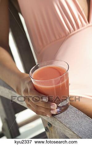 Stock Photo - Beautiful woman holding a glass of juice and sitting on a chair on the beach. Fotosearch