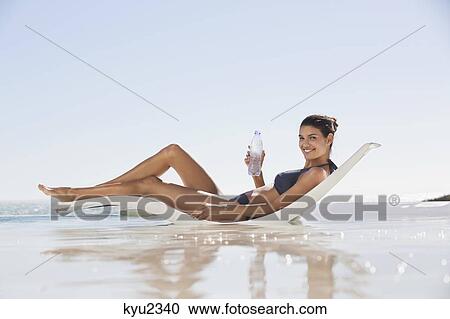 Beautiful woman holding a water bottle while sunbathing on the beach View Large Photo Image Stock Image - Beautiful woman holding a water bottle while sunbathing on the beach. Fotosearch
