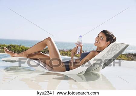 Beautiful woman holding a water bottle while sunbathing on the beach View Large Photo Image Stock Image - Beautiful woman holding a water bottle while sunbathing on the beach. Fotosearch