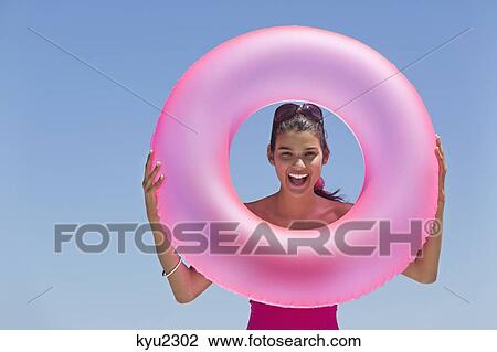 Stock Image - Beautiful woman looking through an inflatable ring on the beach. Fotosearch
