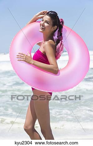 Beautiful woman standing with an inflatable ring on the beach View Large Photo Image Picture - Beautiful woman standing with an inflatable ring on the beach. Fotosearch