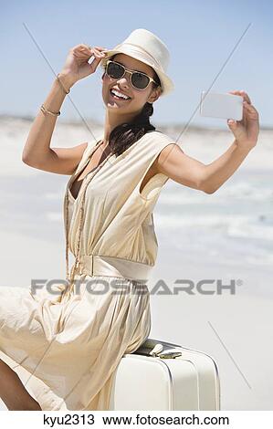 Stock Image - Beautiful woman taking a picture of herself with a cell phone on the beach. Fotosearch