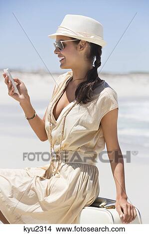 Picture - Beautiful woman text messaging on a cell phone on the beach. Fotosearch