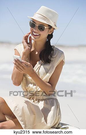 Stock Photography - Beautiful woman using a cell phone on the beach. Fotosearch