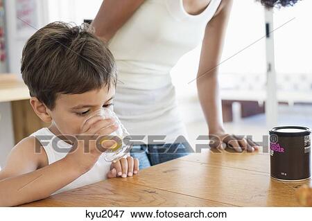 Boy drinking orange juice with his mother standing behind him View Large Photo Image Stock Photo - Boy drinking orange juice with his mother standing behind him. Fotosearch