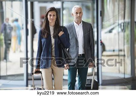 Stock Photo - Business couple pulling suitcases in a hotel lobby. Fotosearch