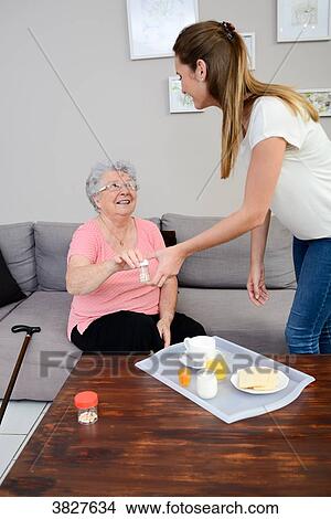 Cheerful young girl giving medicine pills to elderly woman at home. View Large Photo Image Picture - Cheerful young girl giving medicine pills to elderly woman at home.. Fotosearch