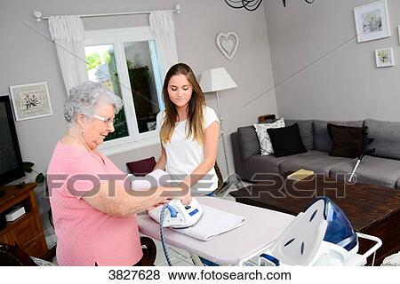 Stock Photo - Cheerful young girl ironing and helping with household chores elderly woman at home.. Fotosearch