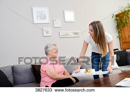 Stock Image - Cheerful young girl serving breakfast to elderly woman at home.. Fotosearch