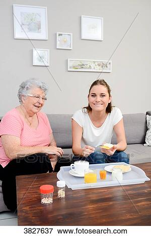 Cheerful young girl serving breakfast to elderly woman at home. View Large Photo Image Stock Photo - Cheerful young girl serving breakfast to elderly woman at home.. Fotosearch