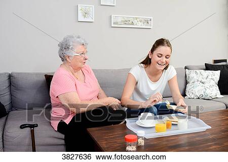 Cheerful young girl serving breakfast to elderly woman at home. View Large Photo Image Stock Photograph - Cheerful young girl serving breakfast to elderly woman at home.. Fotosearch