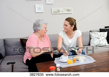 Stock Photography - Cheerful young girl serving breakfast to elderly woman at home.. Fotosearch
