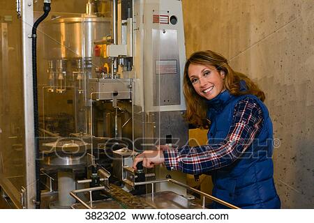 Stock Image - cheerful young woman oenologist adjusting a corking machine in her cellar- Cepage Grenache, Chateauneuf du Pape, cotes du Rhone, France. Fotosearch