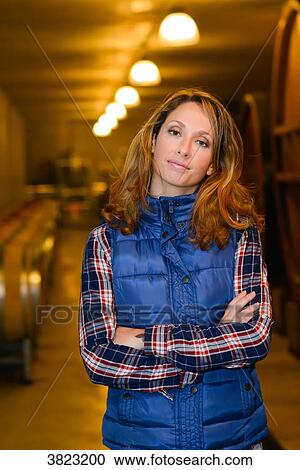 Stock Image - cheerful young woman winery owner posing in her cellar with wine barrel in background- Cepage Grenache, Chateauneuf du Pape, cotes du Rhone, France. Fotosearch