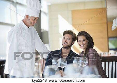 Stock Photo - Chef talking to couple at restaurant. Fotosearch
