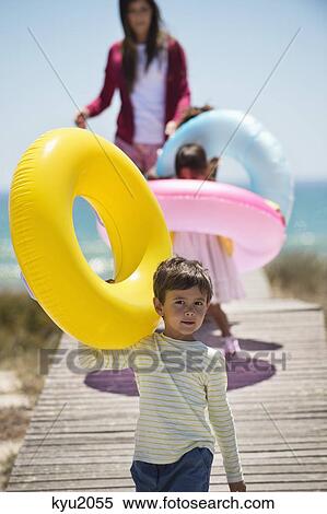 Children with their mother holding inflatable rings on a boardwalk on the beach View Large Photo Image Stock Photography - Children with their mother holding inflatable rings on a boardwalk on the beach. Fotosearch