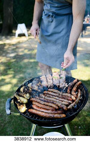 Close up of a barbecue grill with meat and sausages cooking during a summer garden party with people in background. View Large Photo Image Stock Image - Close up of a barbecue grill with meat and sausages cooking during a summer garden party with people in background.. Fotosearch