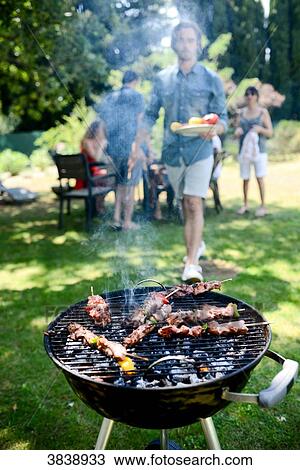 Close up of a barbecue grill with meat and sausages cooking during a summer garden party with people in background. View Large Photo Image Stock Image - Close up of a barbecue grill with meat and sausages cooking during a summer garden party with people in background.. Fotosearch