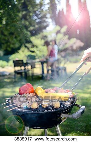 Close up of a barbecue grill with meat and sausages cooking during a summer garden party with people in background. View Large Photo Image Stock Photo - Close up of a barbecue grill with meat and sausages cooking during a summer garden party with people in background.. Fotosearch