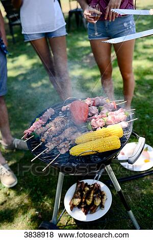 Close up of a barbecue grill with meat and sausages cooking during a summer garden party with people in background. View Large Photo Image Stock Photo - Close up of a barbecue grill with meat and sausages cooking during a summer garden party with people in background.. Fotosearch