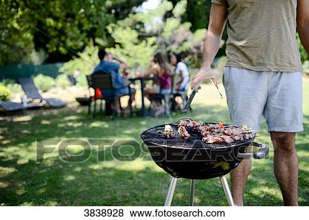 Close up of a barbecue grill with meat and sausages cooking during a summer garden party with people in background. View Large Photo Image Stock Photo - Close up of a barbecue grill with meat and sausages cooking during a summer garden party with people in background.. Fotosearch