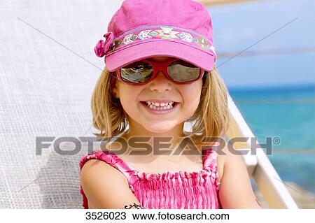 Stock Image - Close-up of little girl smiling with pink sun glasses and cap. Fotosearch