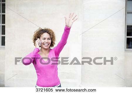 Stock Photography - Close-up of smiling Malagasy woman with phone waving hand. Fotosearch