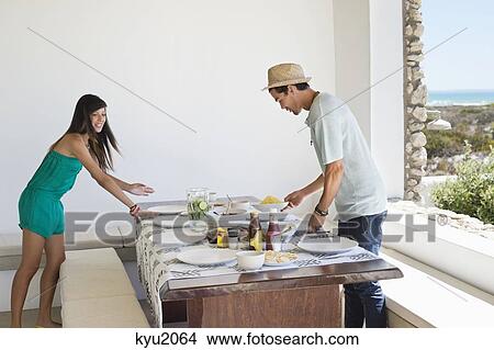 Couple arranging food on a dining table View Large Photo Image Picture - Couple arranging food on a dining table. Fotosearch