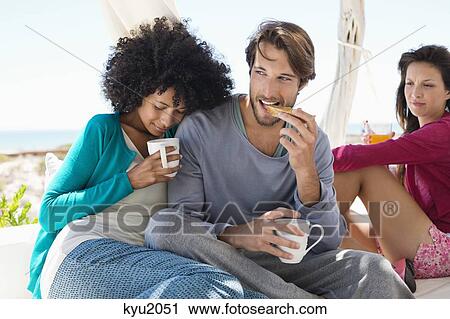 Stock Image - Couple having coffee with their friend in the background. Fotosearch