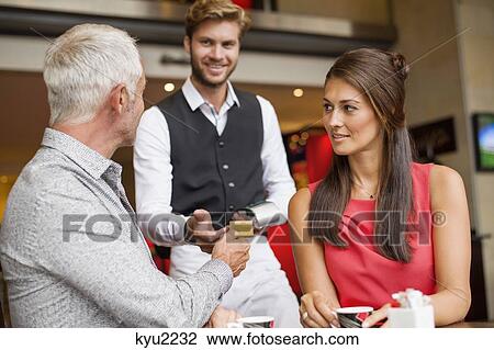 Stock Image - Couple paying with a credit card to a waiter in a restaurant. Fotosearch