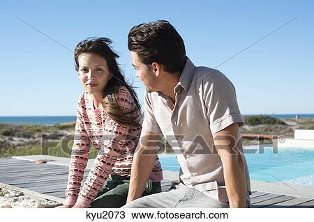 Stock Image - Couple sitting on a boardwalk on the beach. Fotosearch