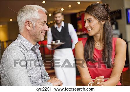Couple smiling in a restaurant with waiter in the background View Large Photo Image Stock Image - Couple smiling in a restaurant with waiter in the background. Fotosearch