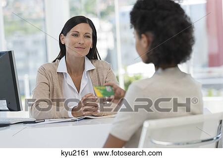 Stock Image - Female doctor looking at a patient holding a health insurance card. Fotosearch