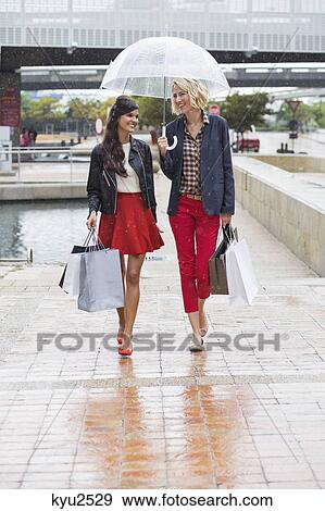 Stock Photo - Female friends walking with shopping bags. Fotosearch