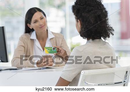 Stock Image - Female patient looking at a health insurance card. Fotosearch